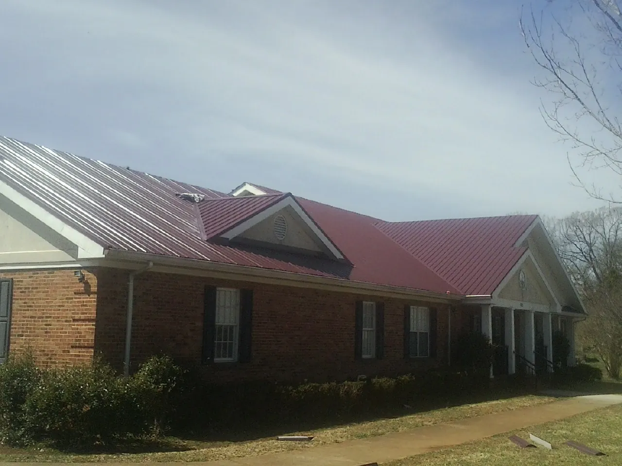 Red metal roof with gabled entries on a long brick building, from a Hail Damage Roof Repair job in Jasper